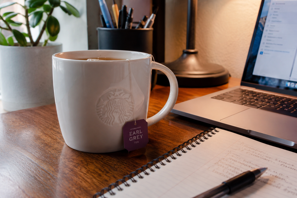 Starbucks Earl Grey tea on a wooden desk beside a laptop and notebook, representing the writing and university life of author Sabastian Gall.